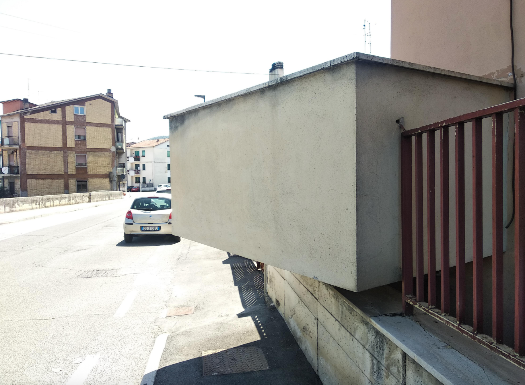 Building structure extends over sidewalk, blocking pedestrian path. Nearby, a car is parked on the street