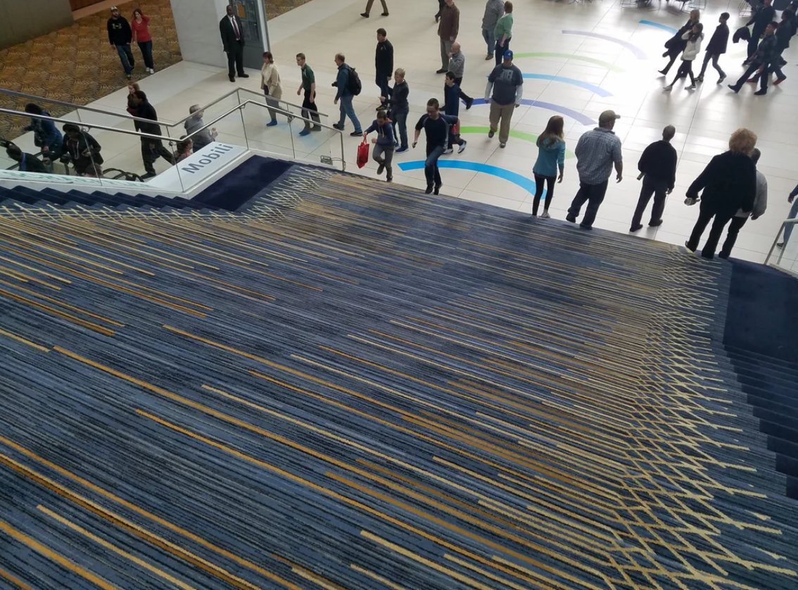 People walking in a large atrium with a patterned carpeted staircase in the foreground