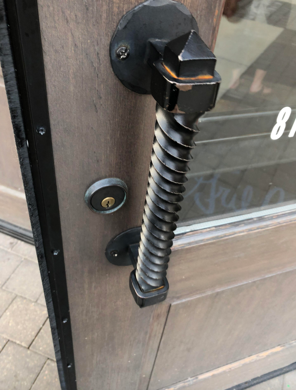 Unique spiral-shaped door handle on a wooden door, above a lock