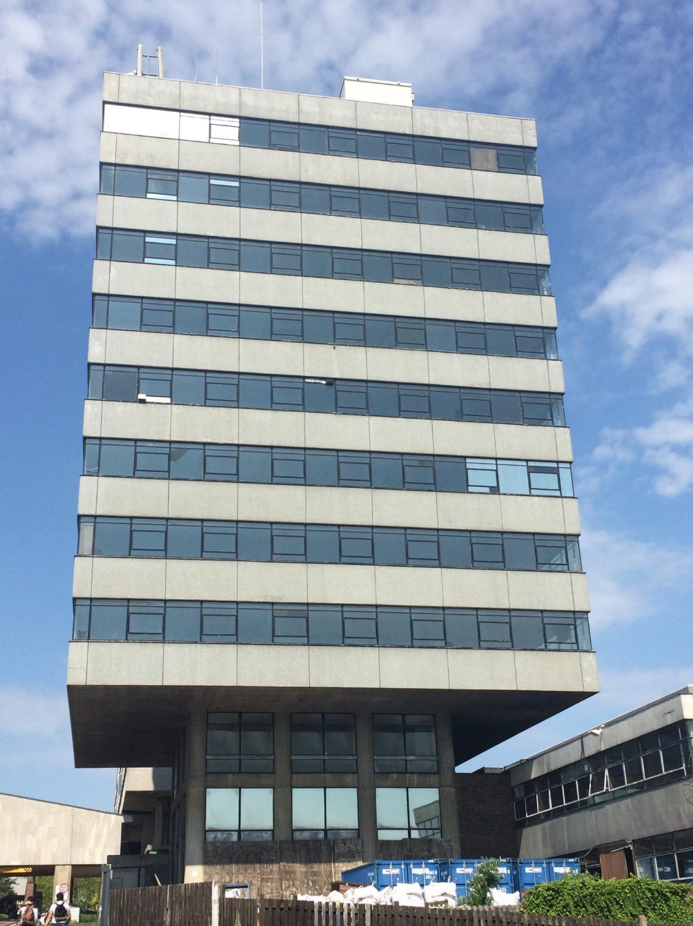 A tall, modern office building with multiple glass windows under a partly cloudy sky