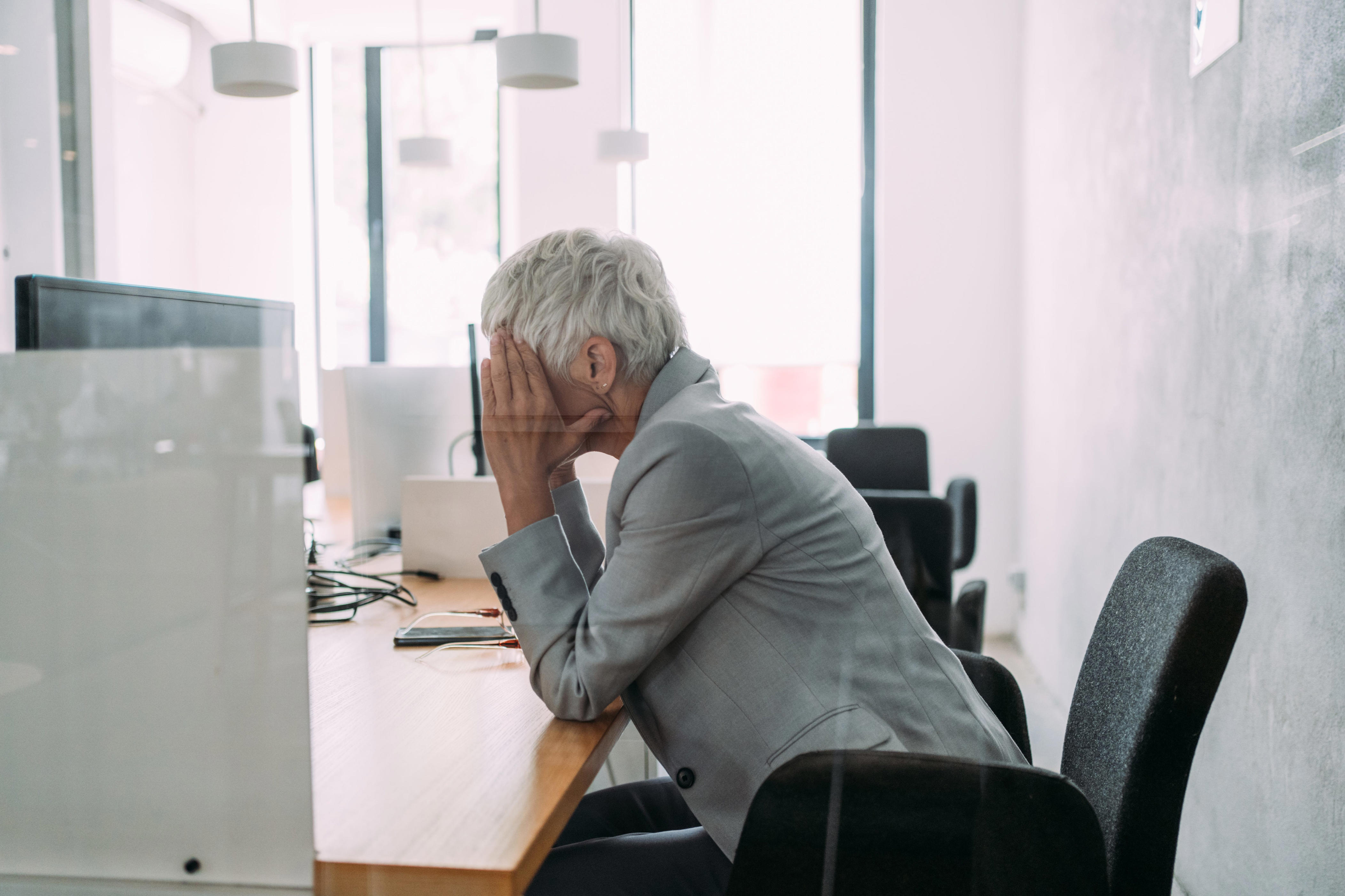 A frustrated person places their head in their hands while sitting at a desk in the office in this photo illustration.