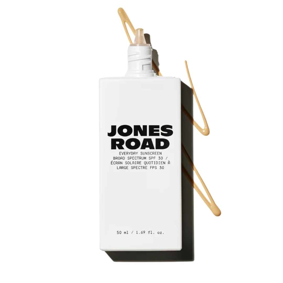 White bottle of Jones Road Everyday Sunscreen with black text and a tinted SPF swatch behind