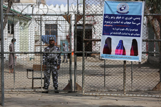 A Taliban prison security guard stands next to a poster ordering women to cover themselves with a Hijab during the distribution of new uniforms' ceremony by the Taliban authorities at a prison in Jalalabad (AFP via Getty Images)