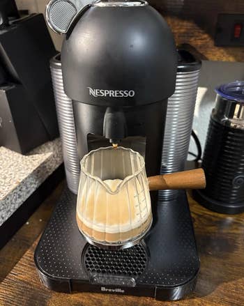 Nespresso machine brewing coffee into a glass pitcher with a wooden handle, placed on a kitchen counter