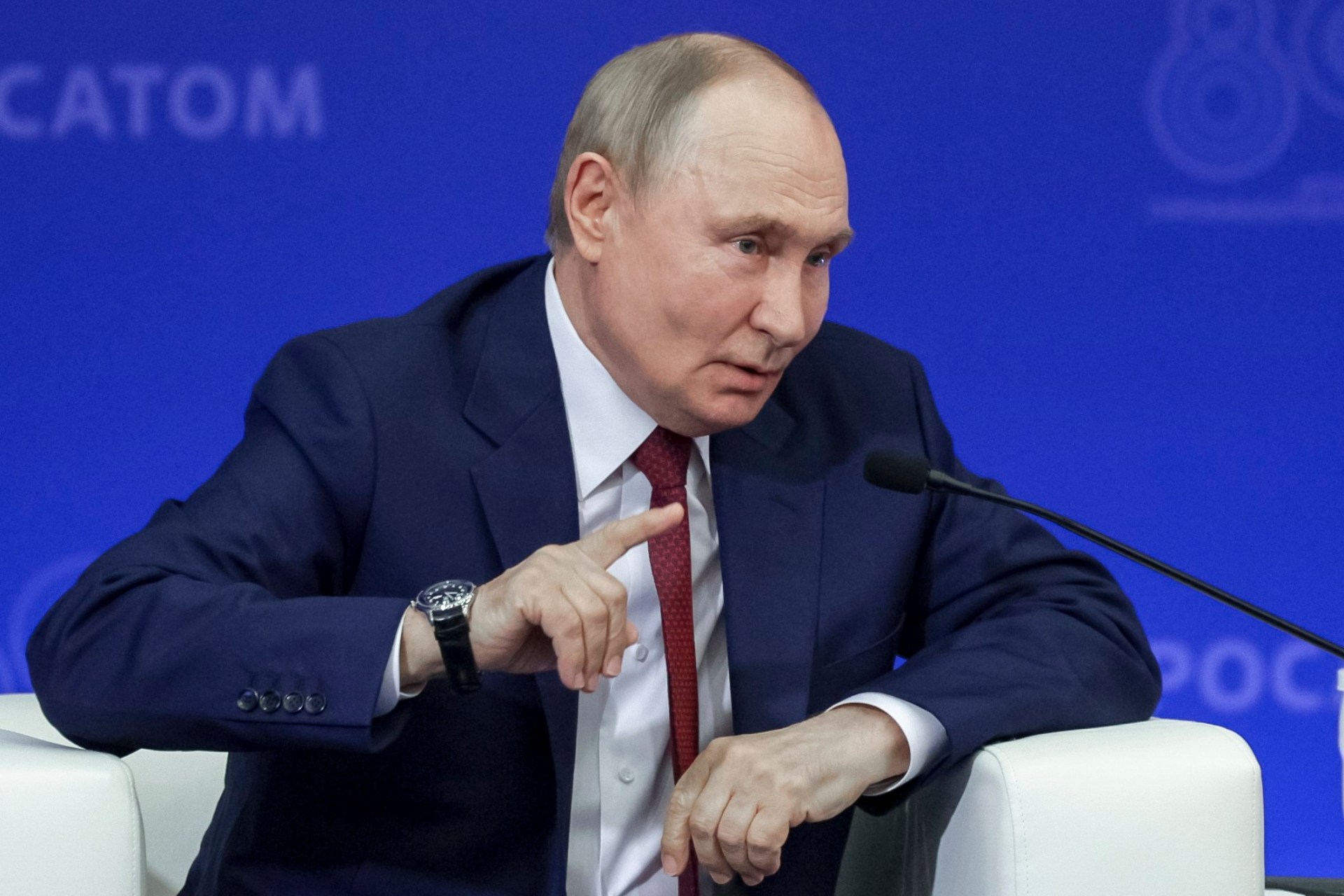 Vladimir Putin gestures towards reporters with a blue background behind him at the Russian Federal Nuclear Centre