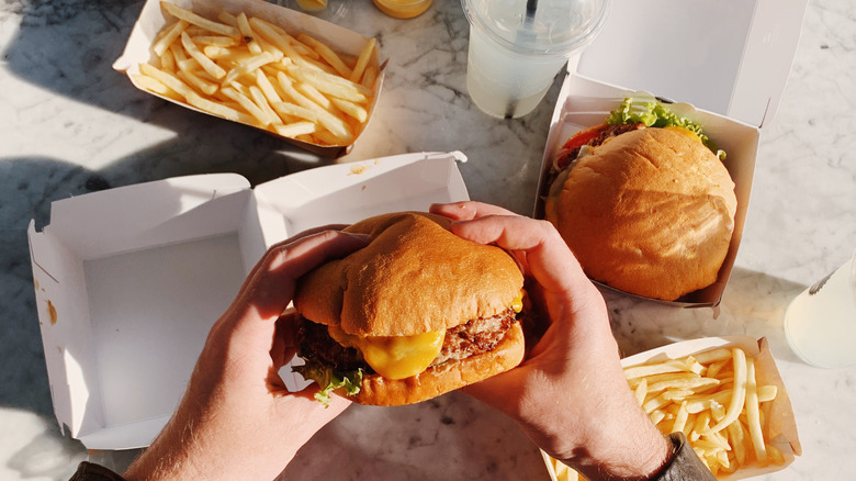 Person holds double cheeseburger with tray of fries.
