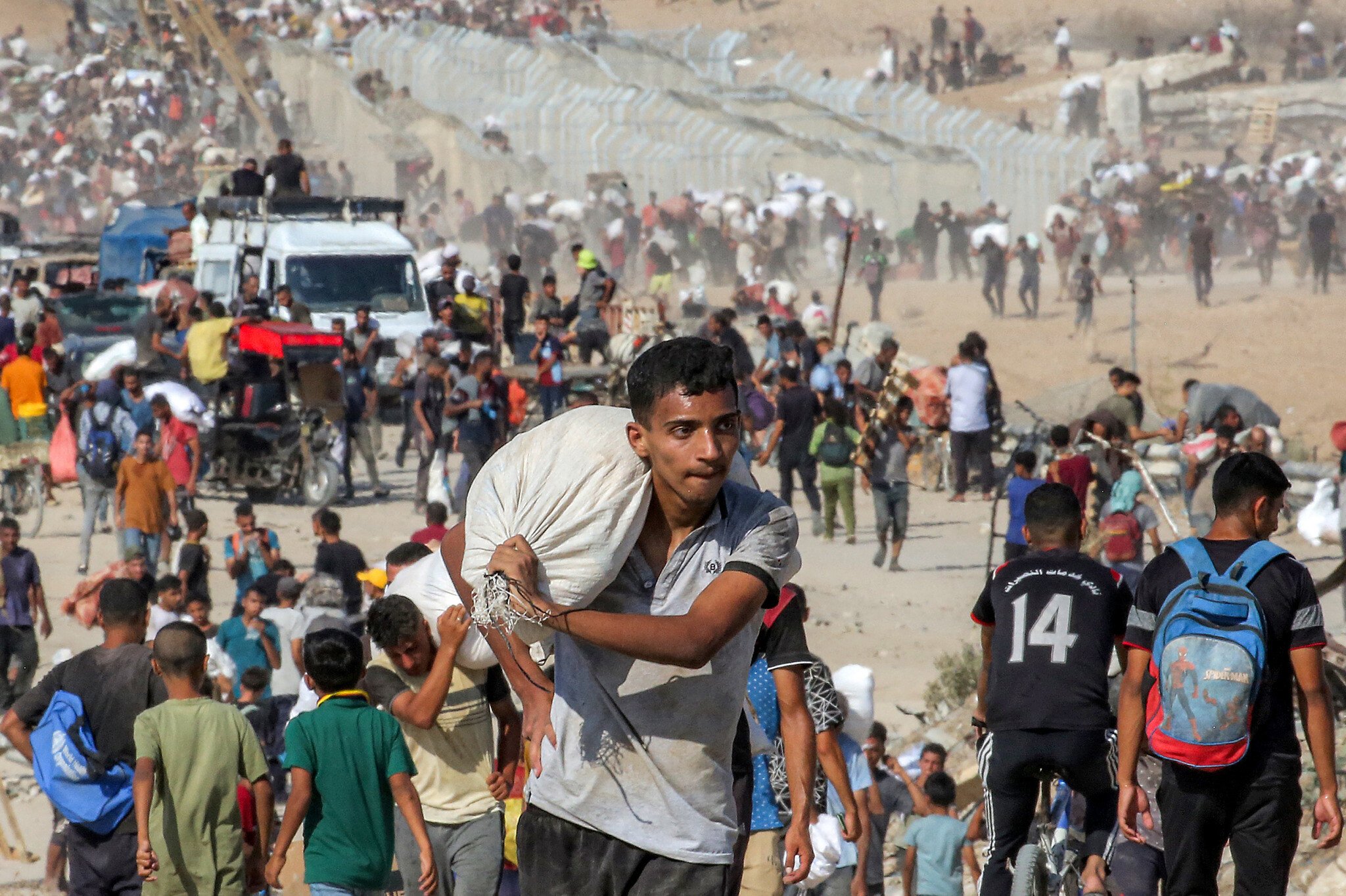 A youth walks with a sack on his shoulder with other people carrying bags of humanitarian aid they received at a distribution center run by the Gaza Humanitarian Foundation (GHF), in the central Gaza Strip, on August 22, 2025. (Eyad BABA / AFP)