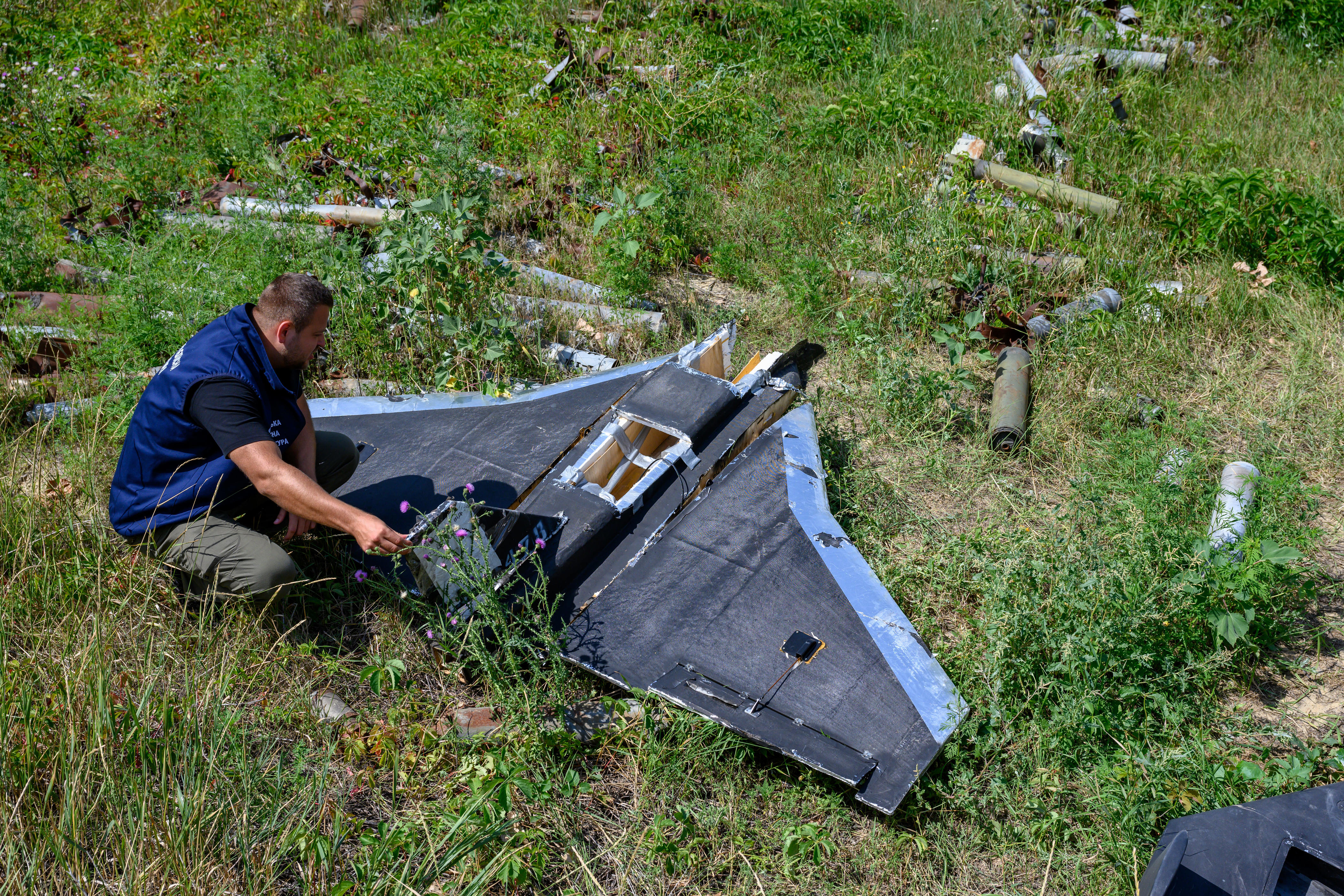 A Ukrainian official looks at the wreckage of a Gerbera drone, designed as a decoy for the Russian Shahed, in a grass field.