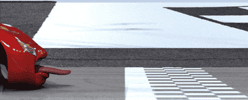 Animated car with eyes and a tongue-like expression approaches a finish line, evoking a playful, cartoonish scene from an animated movie