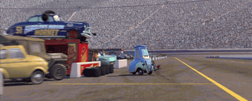 Animated scene from "Cars" showing characters Luigi and Guido changing tires at a racetrack. Stands are full of fans