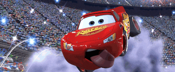 Animated race car with expressive eyes, Lightning McQueen, joyfully soars over a cheering stadium crowd in a scene from a movie