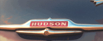 "HUDSON" emblem on the rear of a vintage car, reflecting sunlight off the metallic finish