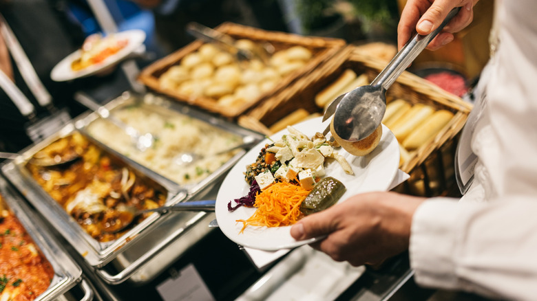 A diner fills their plate with dolmas and salads at a buffet.