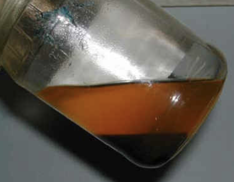 Hiện tượng tách lớp của xăng ethanol, lớp trên (màu cam) là xăng bị giảm nồng độ ethanol, lớp cặn đen ở dưới là hỗn hợp ethanol và nước. Ảnh: BP