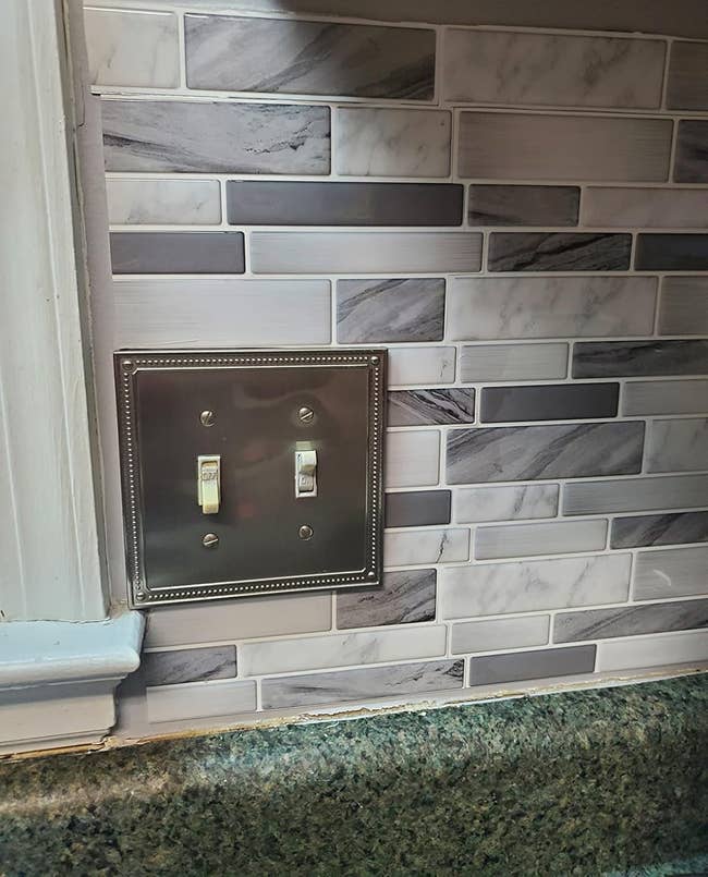 Decorative tile backsplash with a metal light switch cover in a kitchen setting, showcasing a modern, stylish design