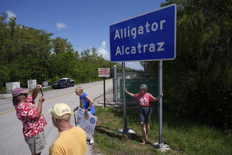 People take pictures in front of a sign reading Alligator Alcatraz as passerby, some opposed, some in support, visit the entrance to an immigration detention center in the Florida Everglades, Thursday, Aug. 28, 2025, in Collier County, Fla. (AP Photo/Rebecca Blackwell)