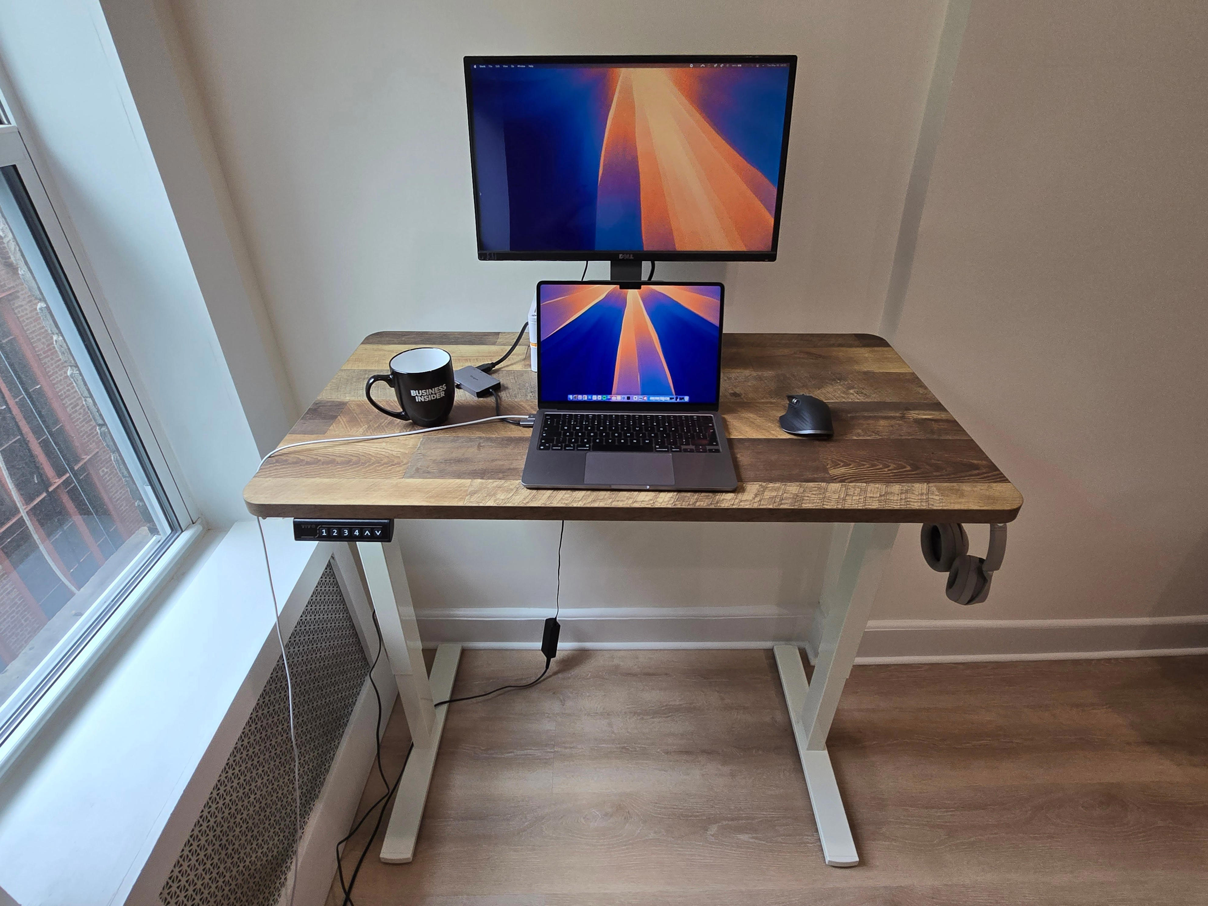Vivo standing desk with wood grain detail with laptop. monitor and coffee cup on the desk