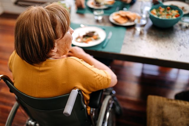 Stock photo of a senior woman sitting in wheelchair at table during breakfast in nursing home.
