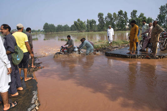 Villagers help a milkman cross a flooded road on the outskirts of Sodhra town in Pakistan on 29 August 2025 (AP)