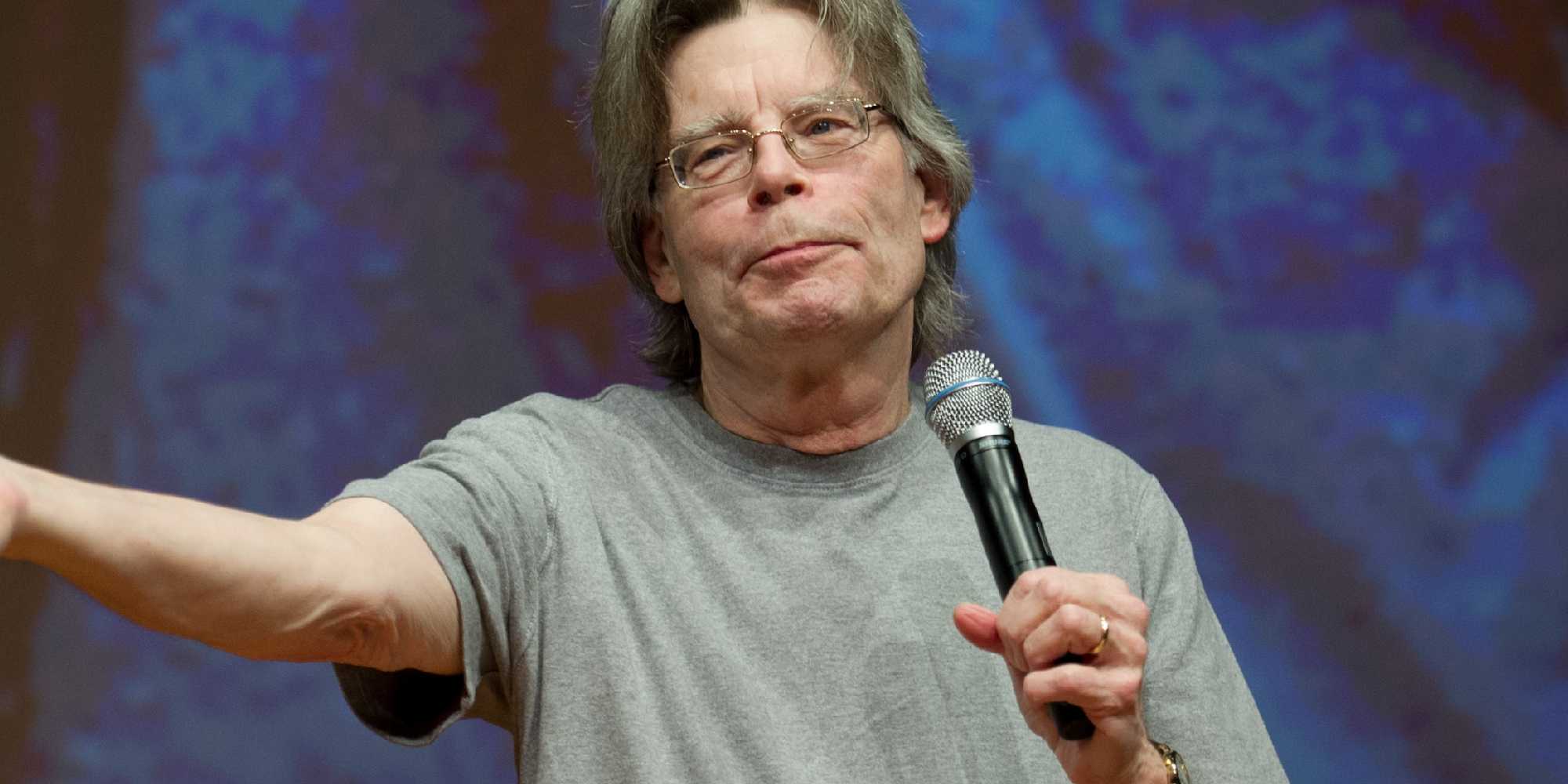 Stephen King with a microphone holding out his arm