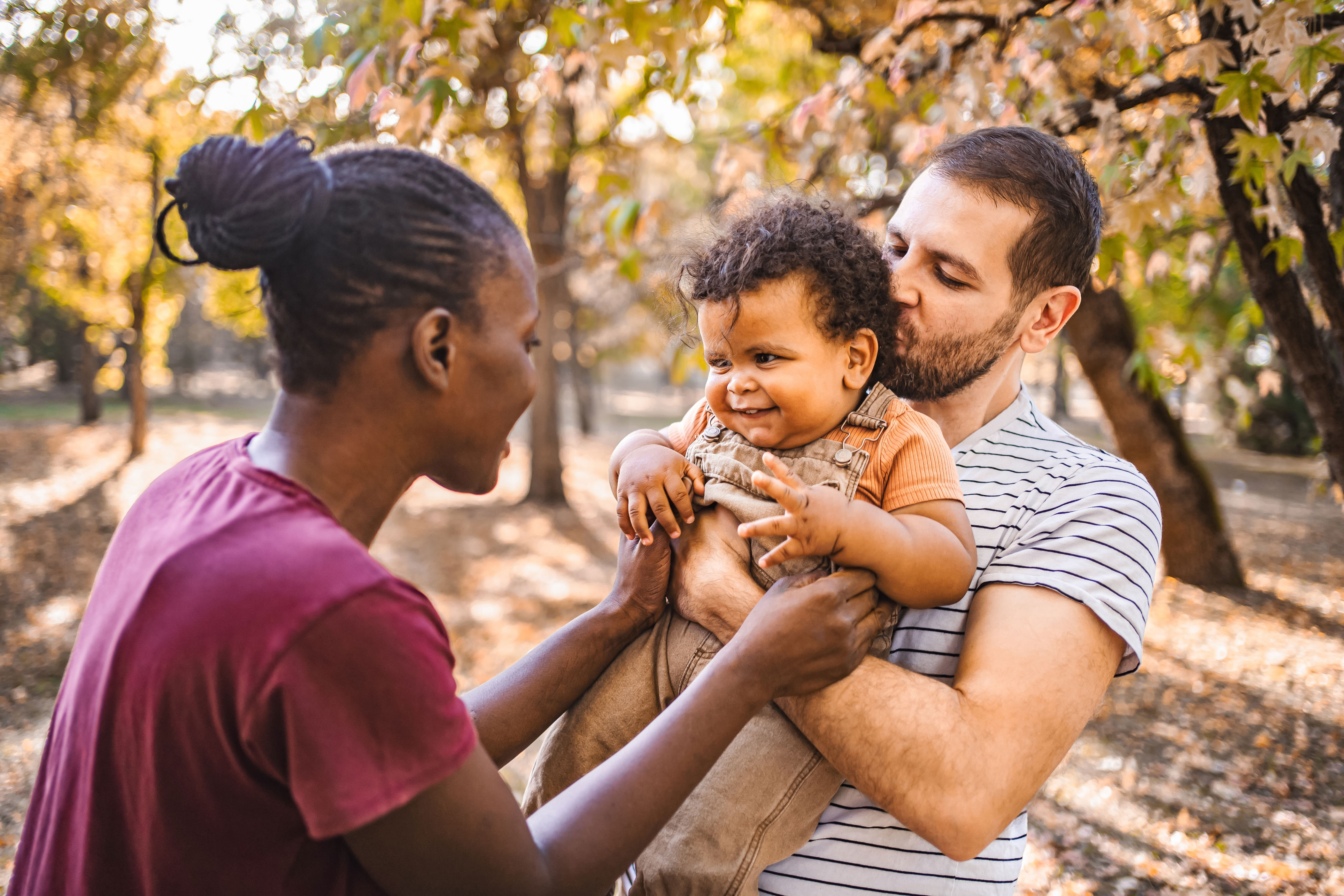 A joyful couple shares a moment outdoors, holding a smiling baby between them, conveying love and happiness