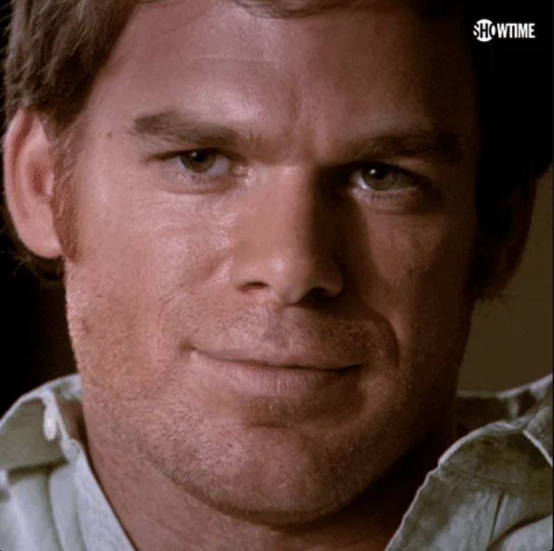 Man with short hair and stubble looks at the camera, wearing a collared shirt.
