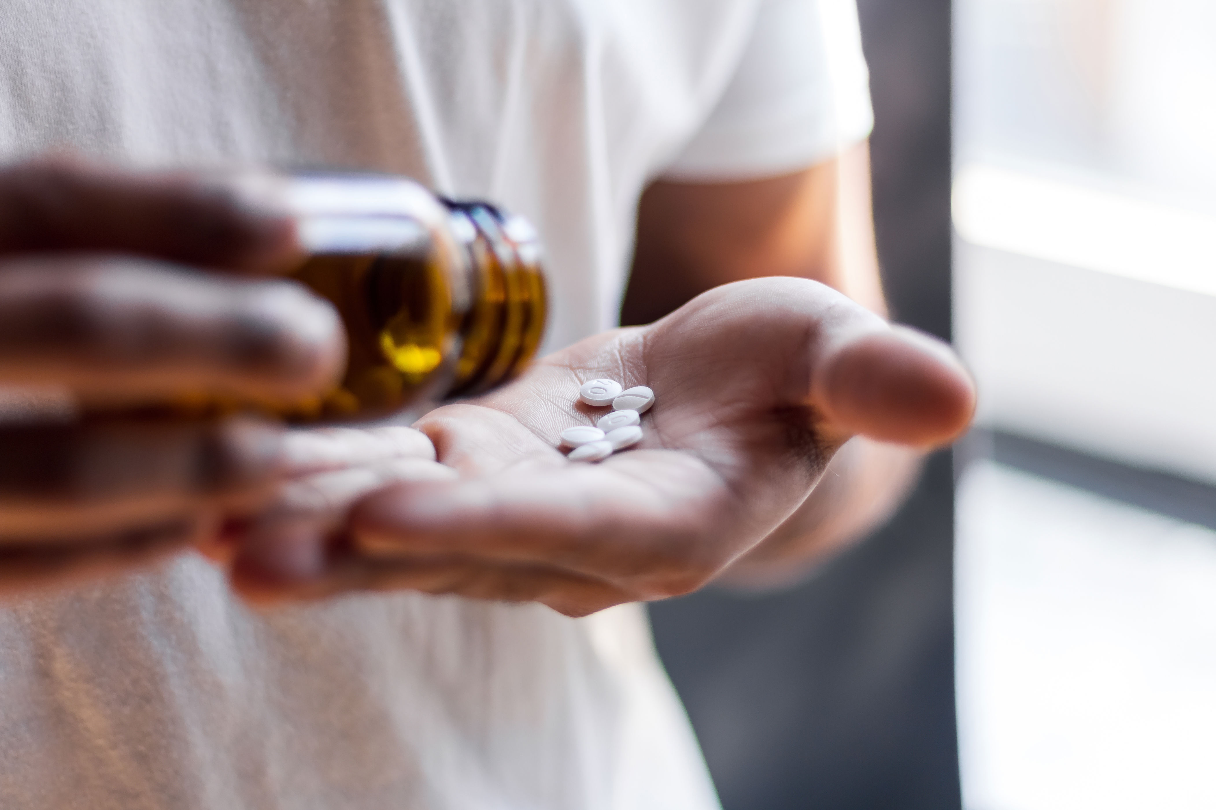 A person pours several white pills from a brown bottle into their hand, suggesting medication or supplements