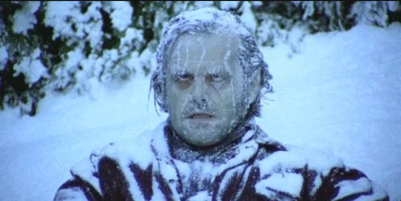 A person is frozen and covered in snow, with a distressed expression, sitting outdoors