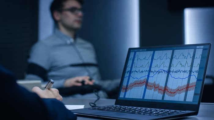 A person taking a polygraph test, with graphs displayed on a laptop screen showing fluctuating lines