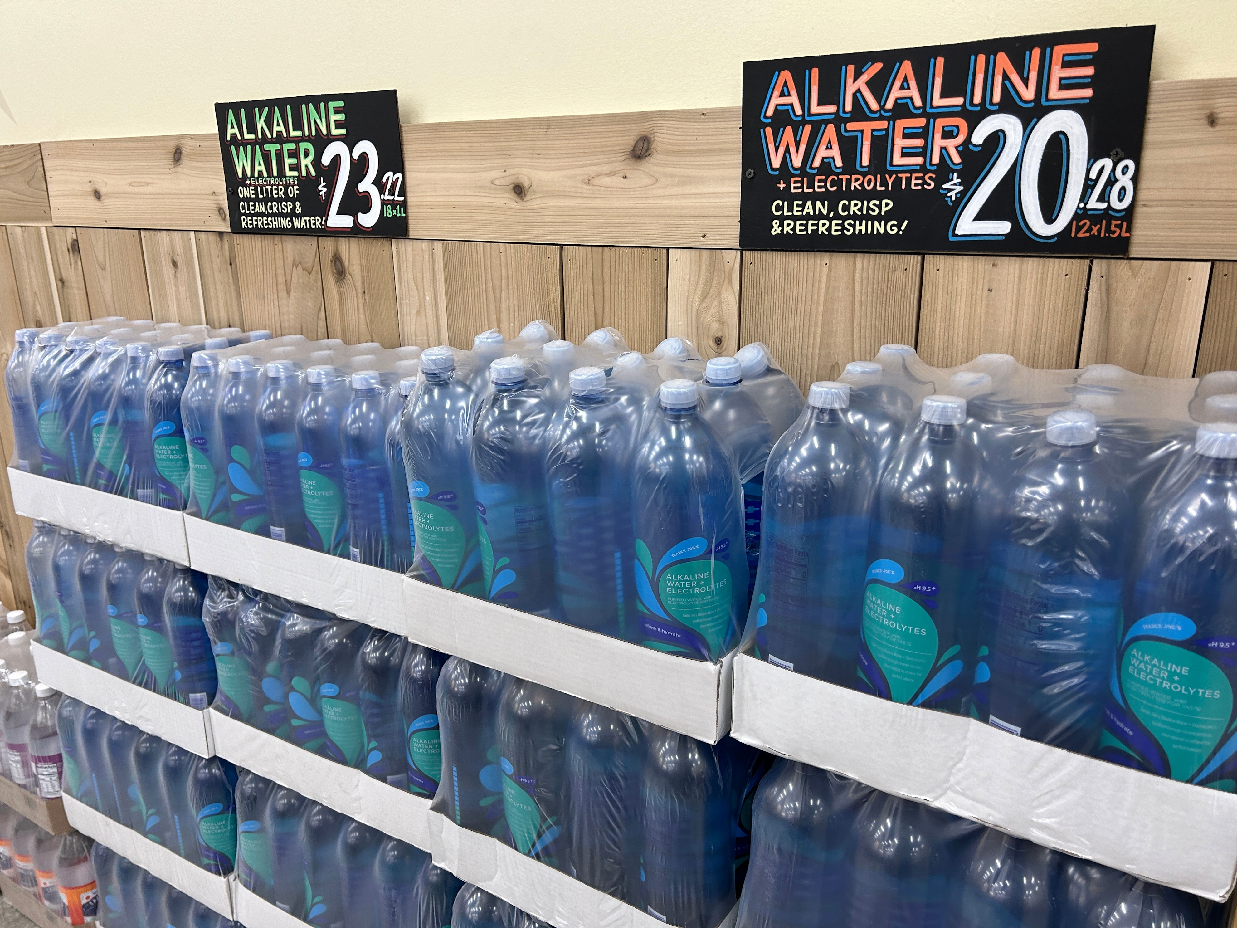 Bottles of alkaline water are displayed on wooden shelves with a price tag of 20.28 for a 12-pack of 1.5-liter bottles