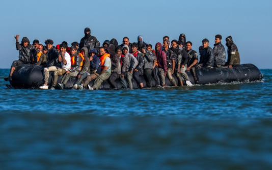 Migrants sit on a dinghy as they wait to cross the English Channel from France on August 25 - Carl Court/Getty Images