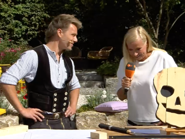 Andrea Kiewel versucht beim „ZDF-Fernsehgarten“ im Gespräch mit Zimmerermeister Laurin Bock lustig zu sein.