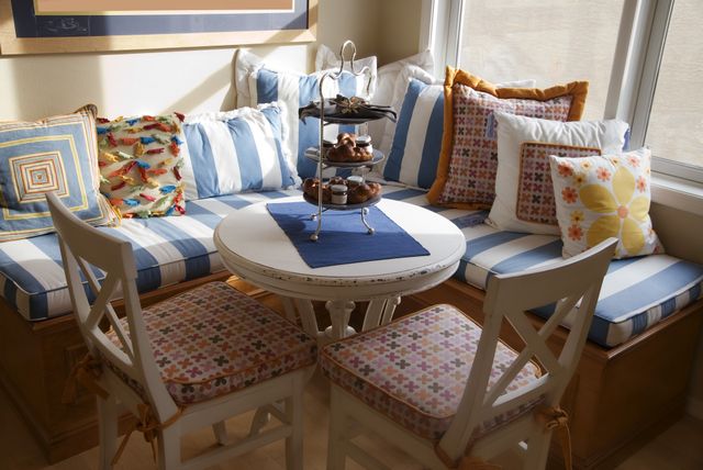 A cozy breakfast nook with a circular table cushioned bench seating two chairs and a threetiered tray on the table