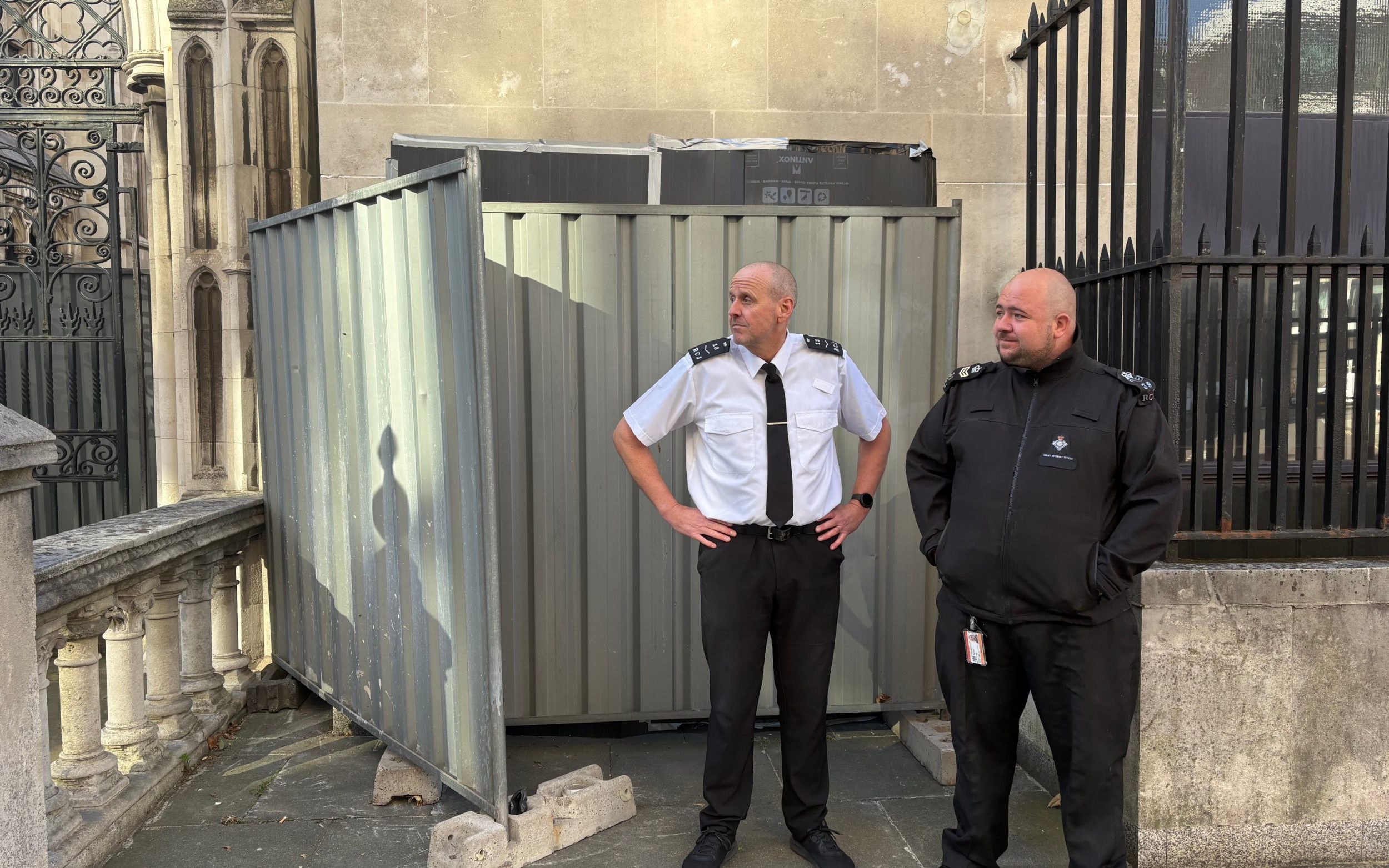 A view of security guards standing at the spot outside the Royal Courts of Justice, near to the external wall of the Queen's Building, by large sheets of black plastic and two metal barriers which are covering a new work understood to be by the street artist Banksy