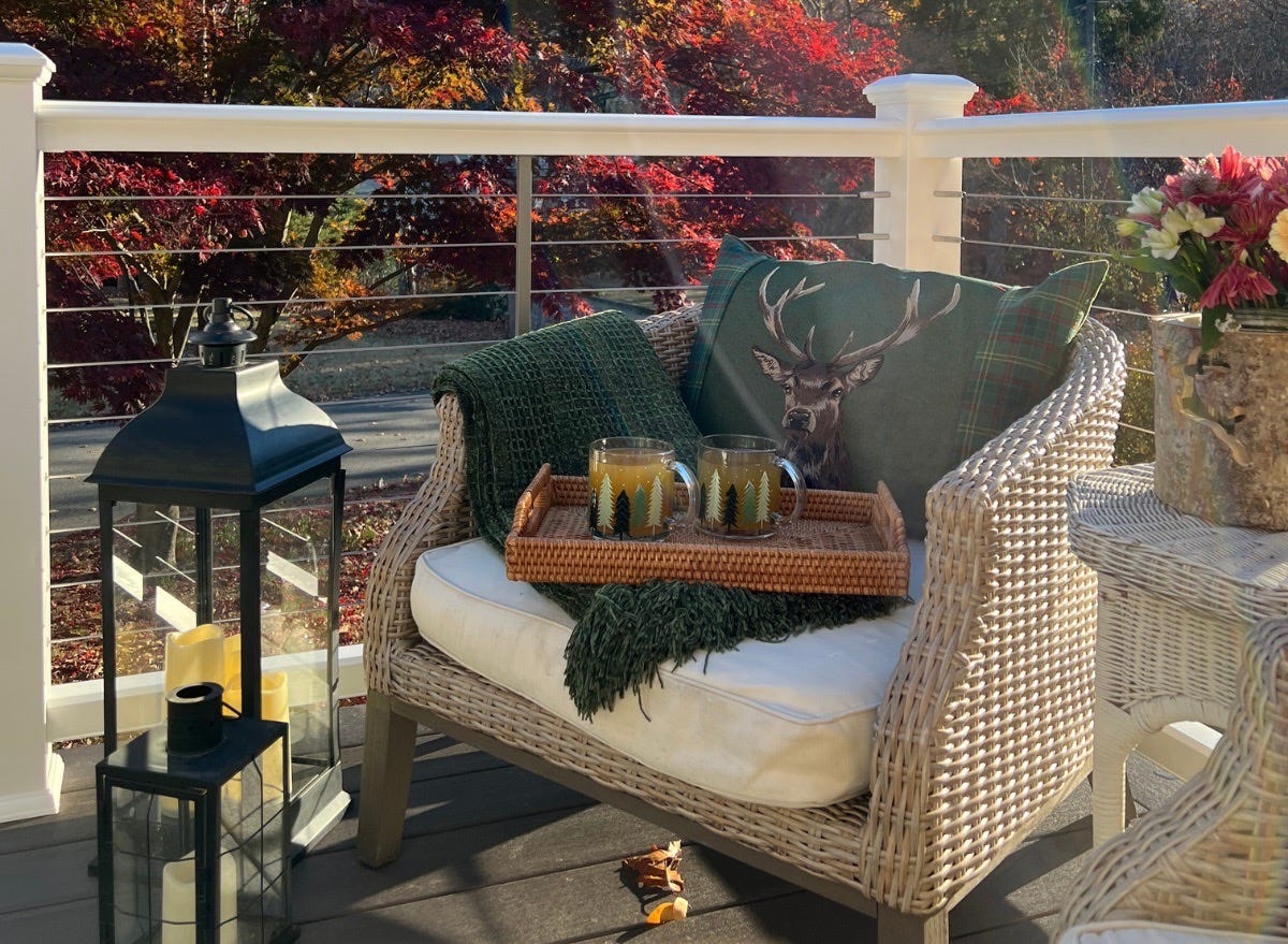 Chair on front porch with plaid blanket and tray of drinks on it with fall foliage behind