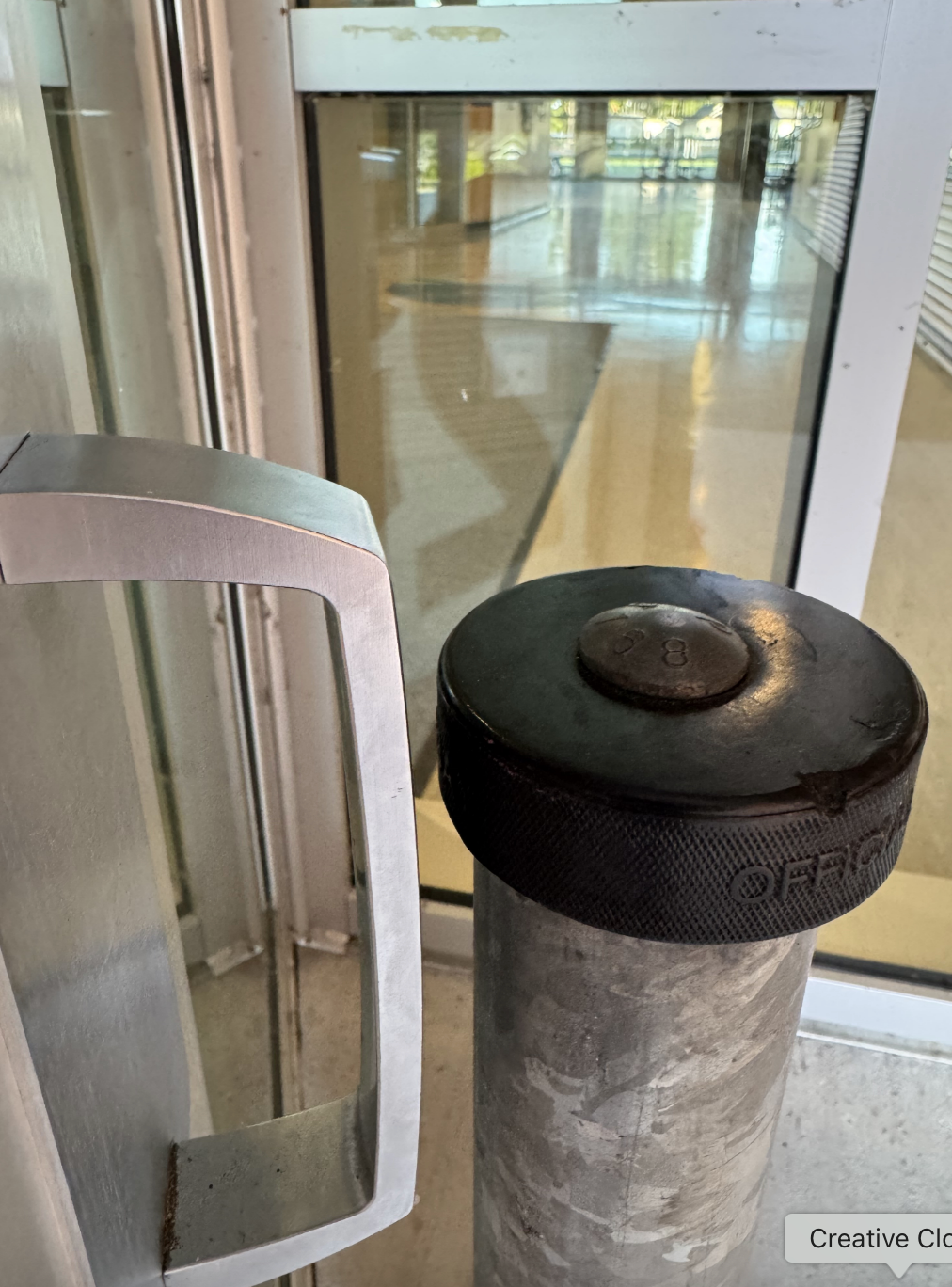 Automatic door handle beside a metal bollard with a rubber cap inside a building entrance. Reflections are visible on the glass doors