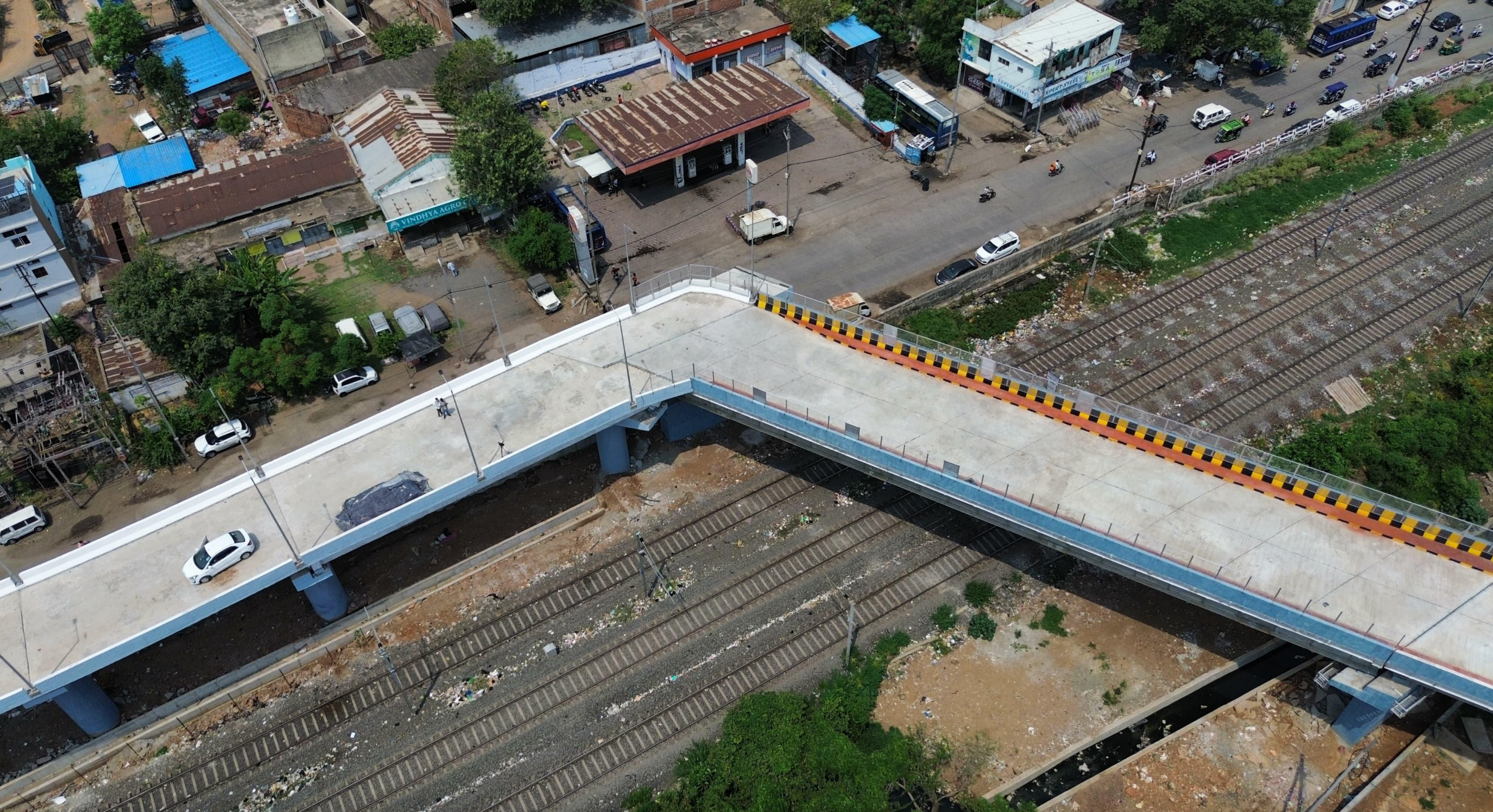 Aerial view of a road bridge crossing over railway tracks, with nearby buildings and parked vehicles visible