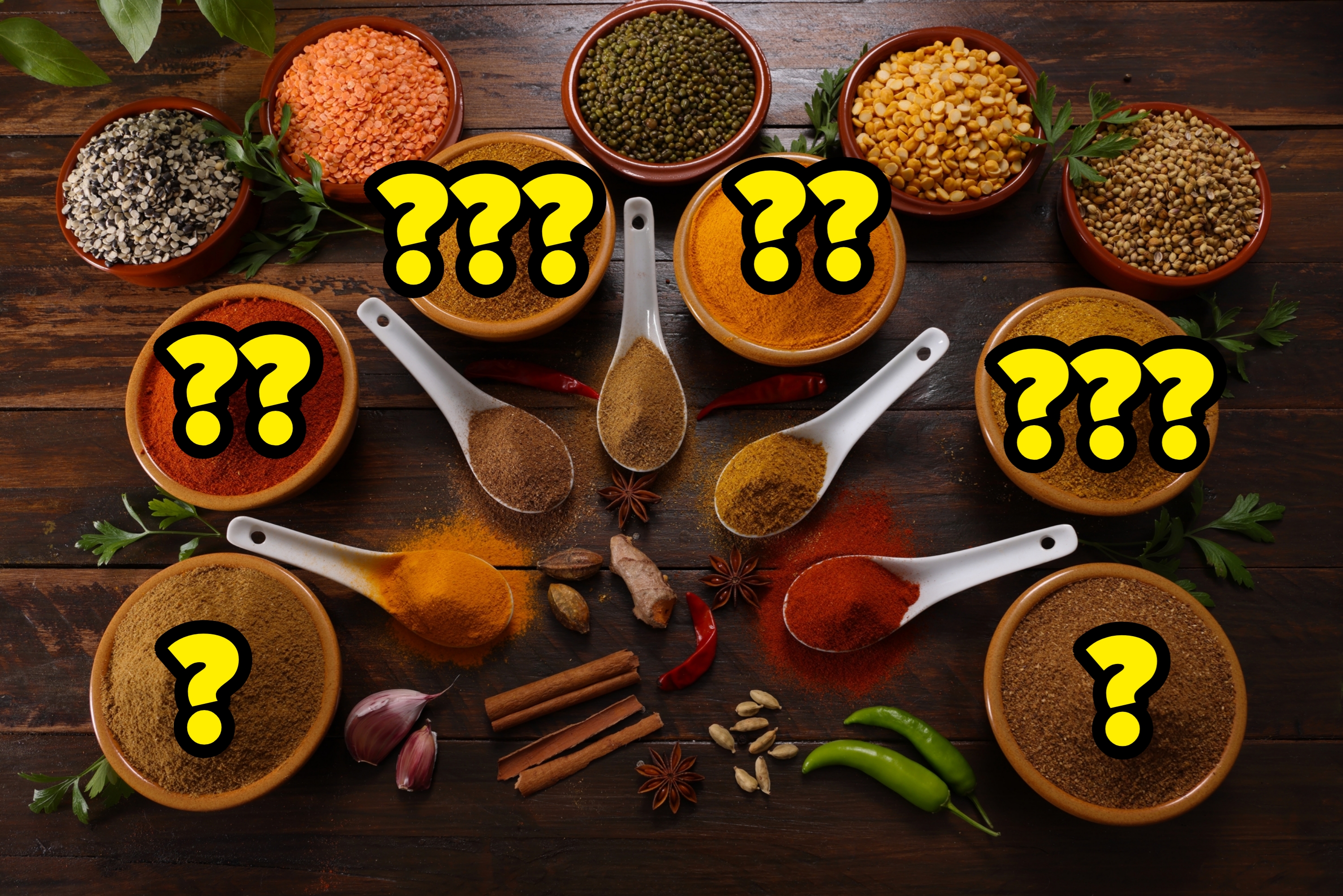 Assorted spices and herbs arranged in bowls and on spoons, including chili, turmeric, and cumin, with fresh garlic, ginger, and peppers on a wooden table