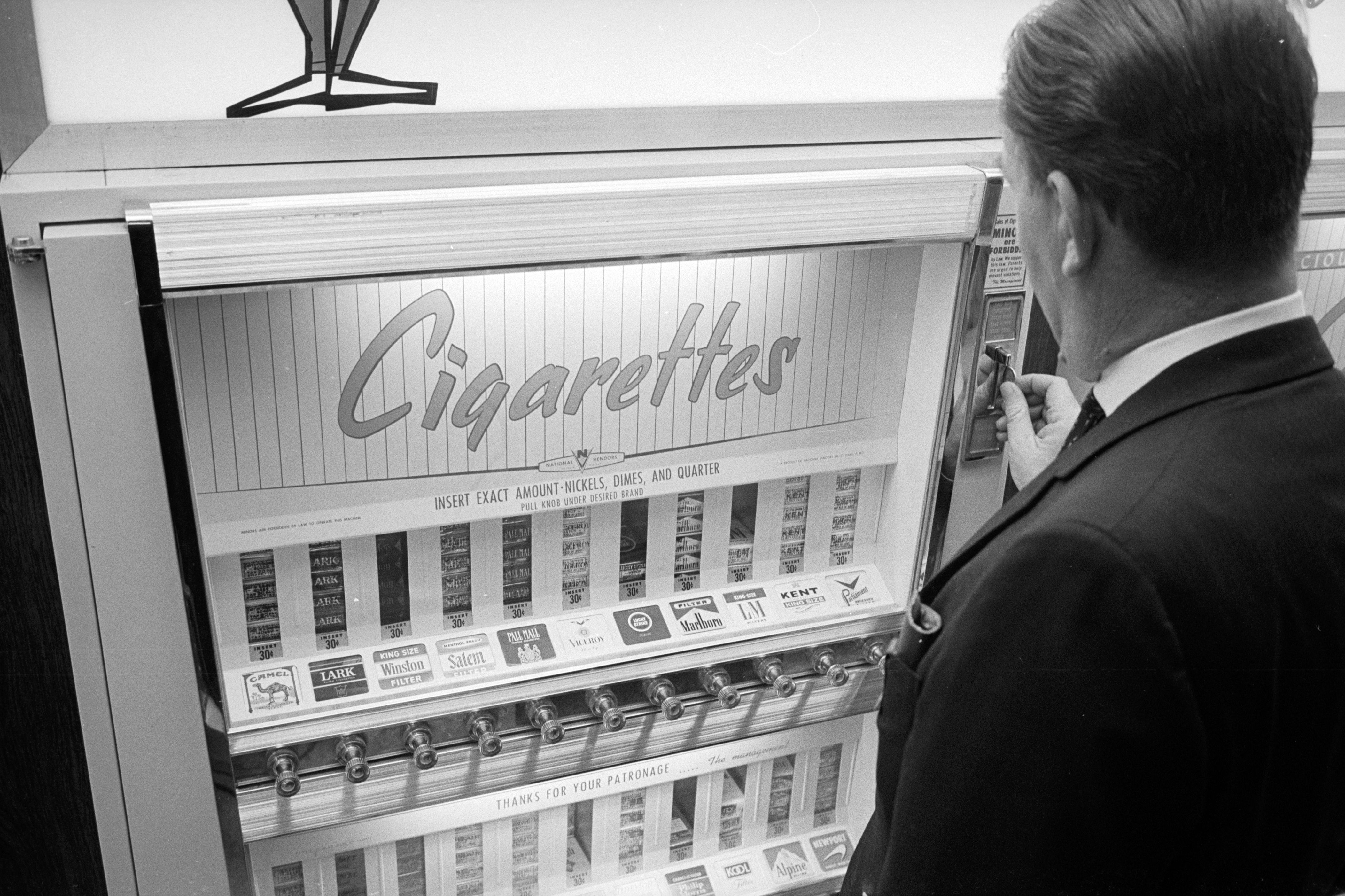 Man using vintage cigarette vending machine with various brand options displayed