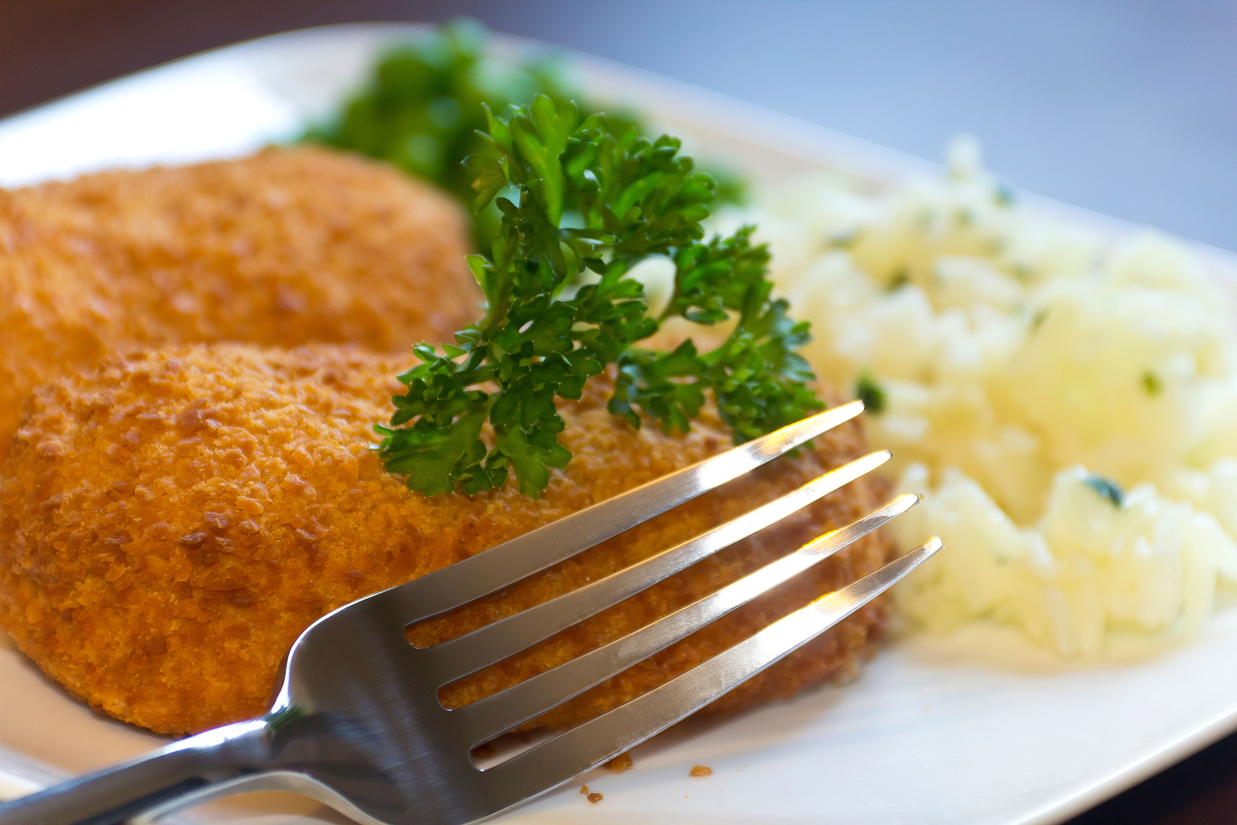 Fork over crispy breaded fish fillets garnished with parsley, served with a side of mashed potatoes