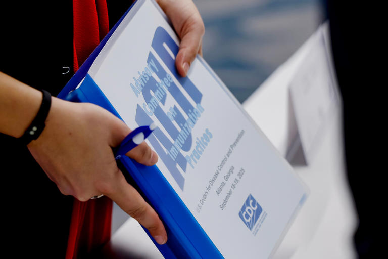 A CDC staffer holds a program notebook during an ACIP meeting.