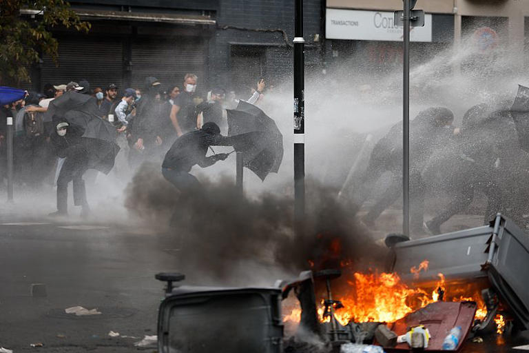 Protesters of the "Block Everything" movement take cover of a water canon behind umbrellas in Lille, 10 September, 2025 AP Photo