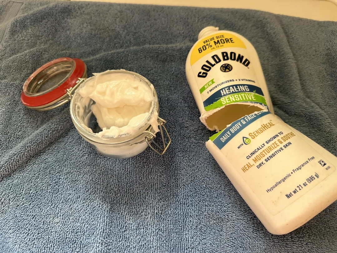 Open jar of cream and a tube of Gold Bond lotion on a towel