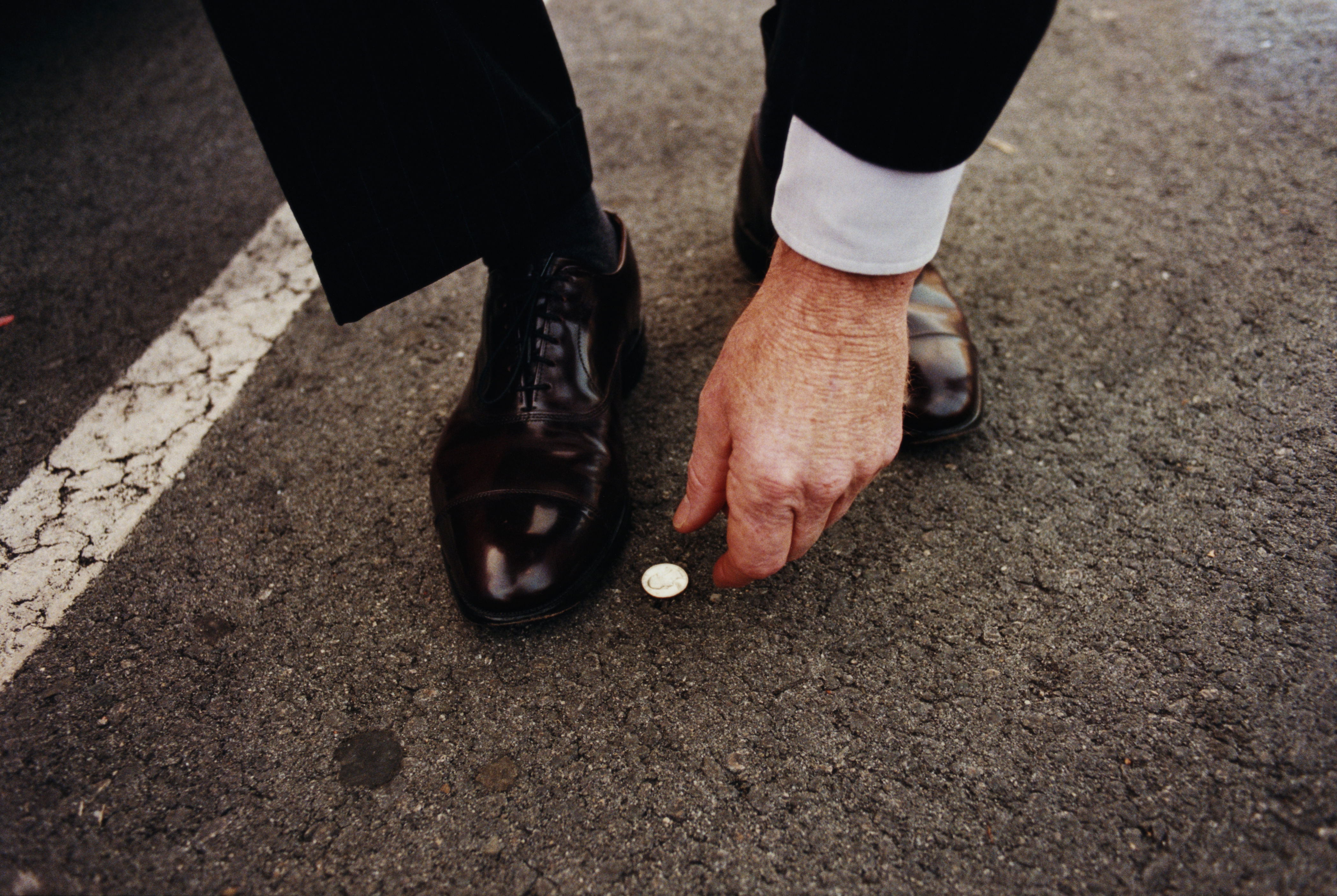 Person in formal attire picking up a small coin from the asphalt