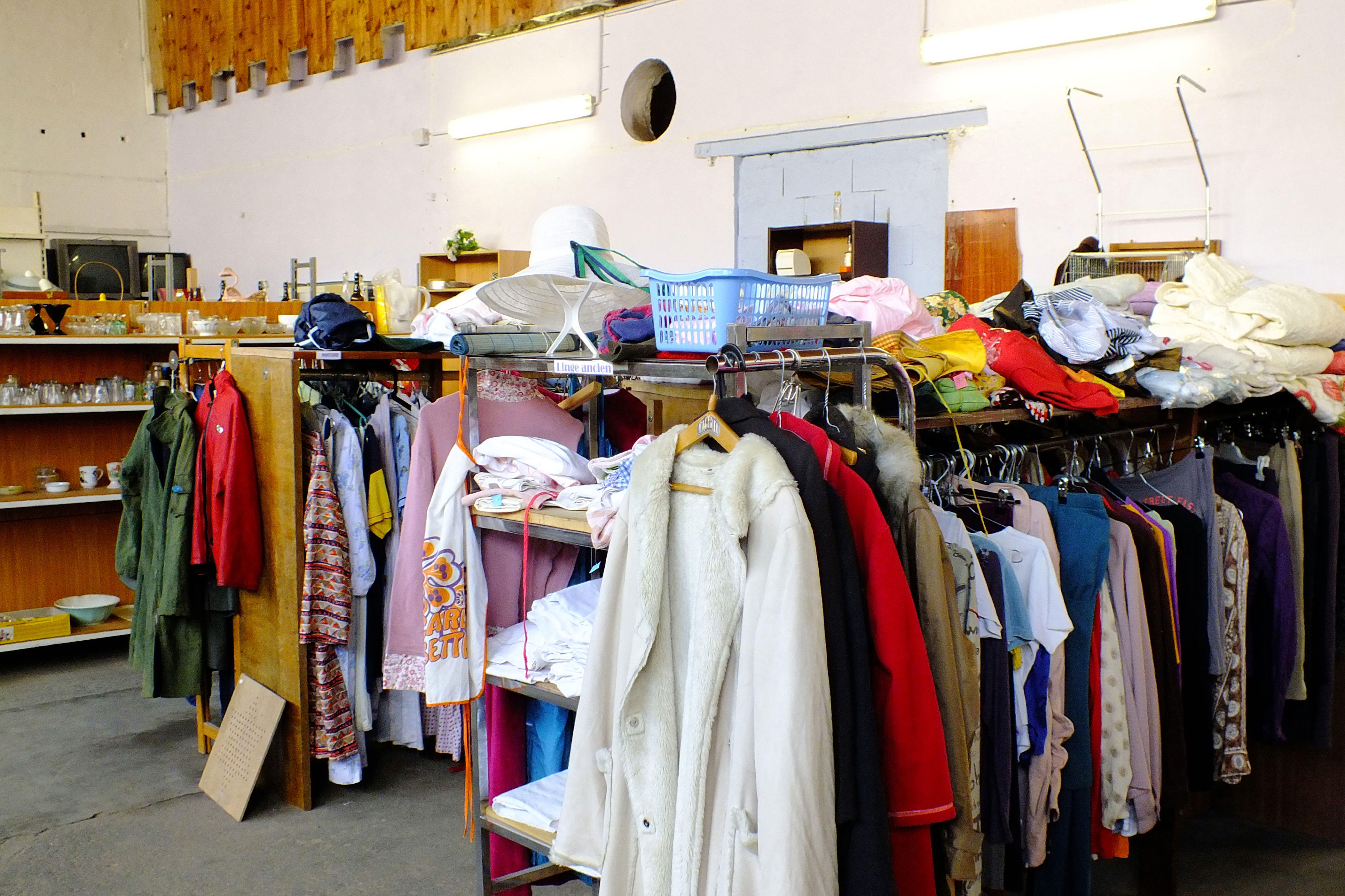 Thrift store interior with racks of assorted clothing and shelves of various household items and decor