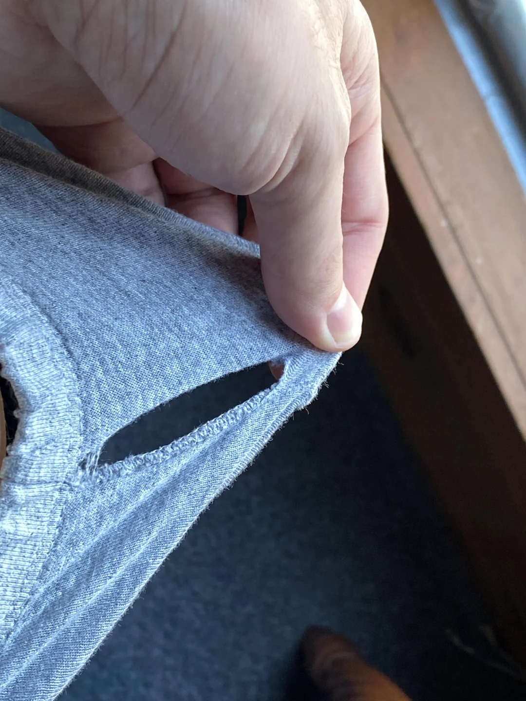 Person holding a torn piece of fabric on a piece of clothing