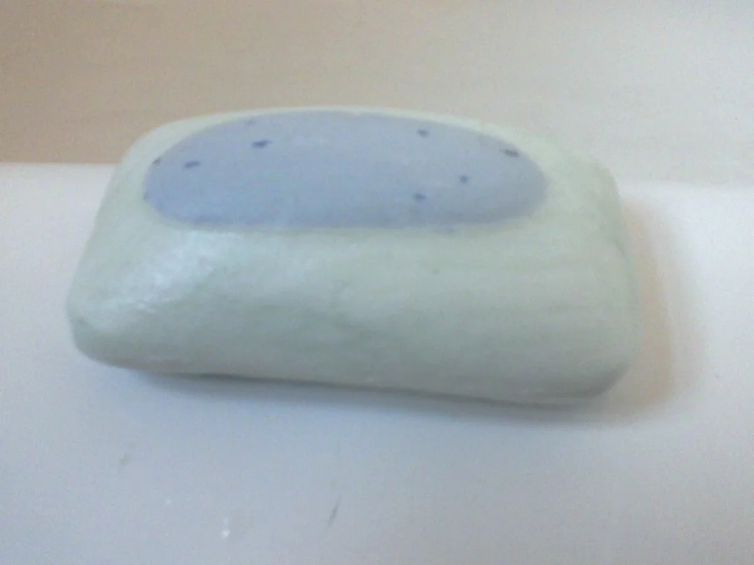 Smooth soap bar with a lavender center and speckled spots, resting on a flat surface