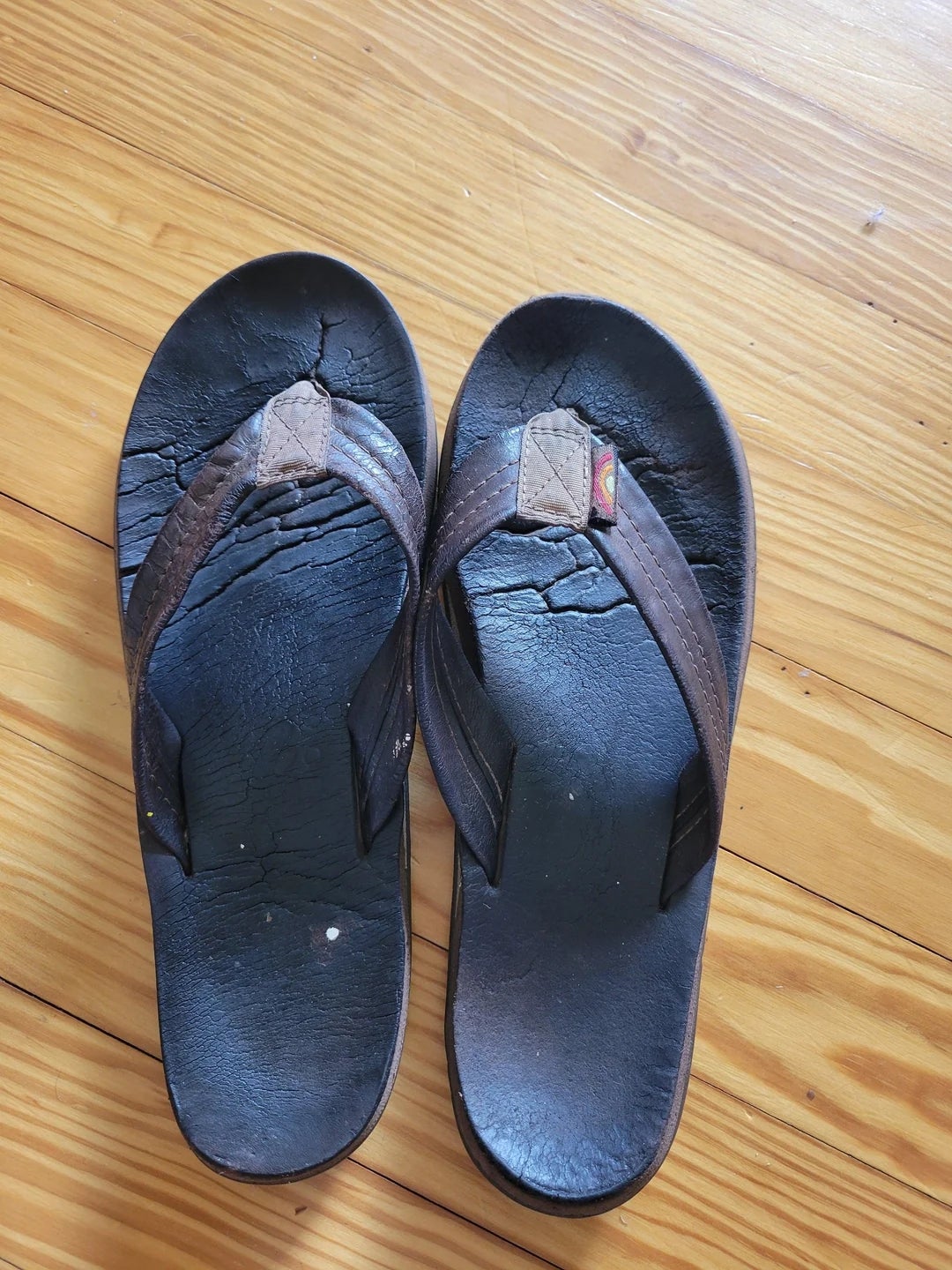 Worn-out flip-flops with cracked soles, placed on a wooden floor