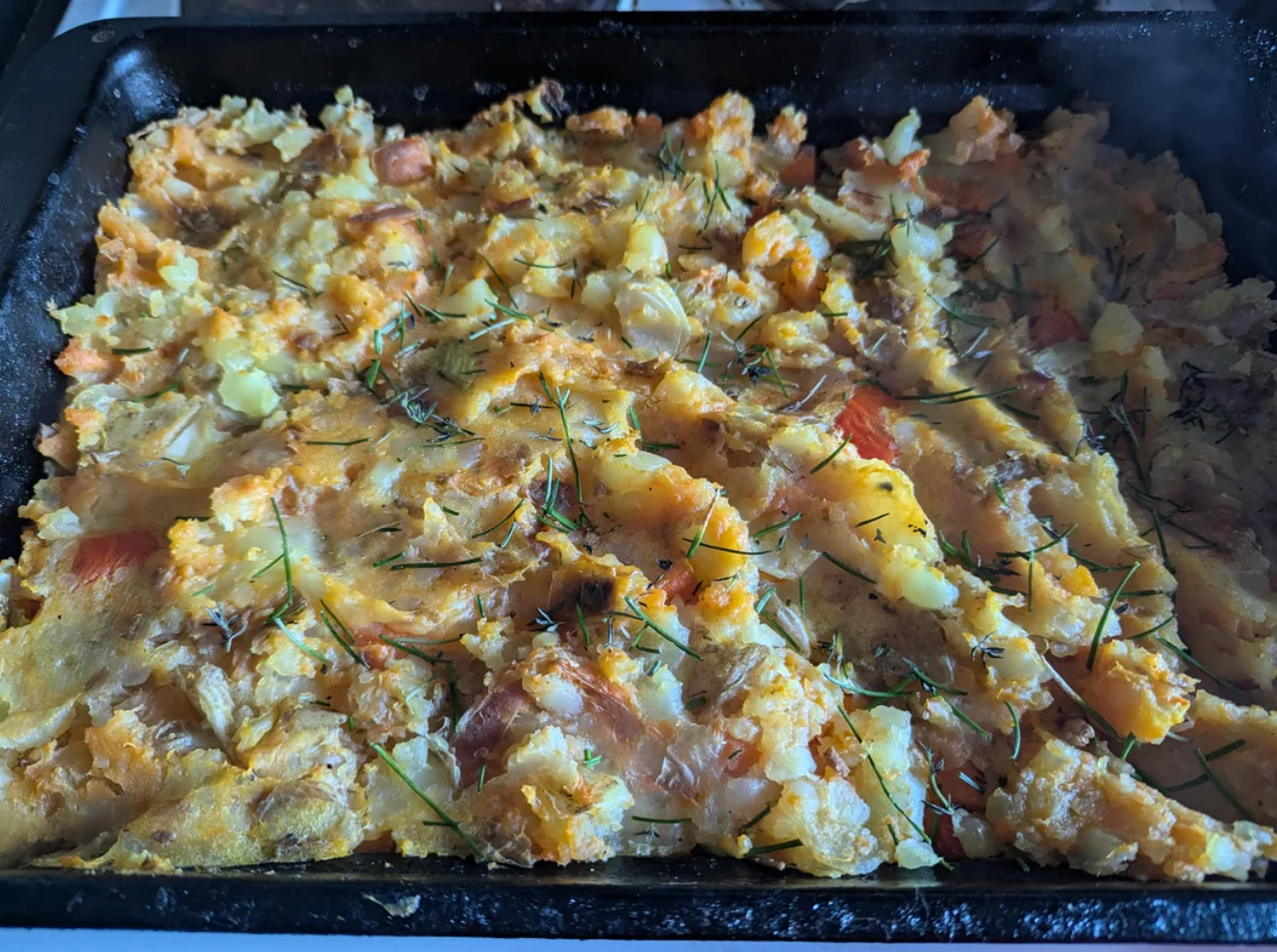 Baked dish with potatoes, cabbage, and herbs, appearing rustic and hearty. Steam rising suggests it's freshly cooked