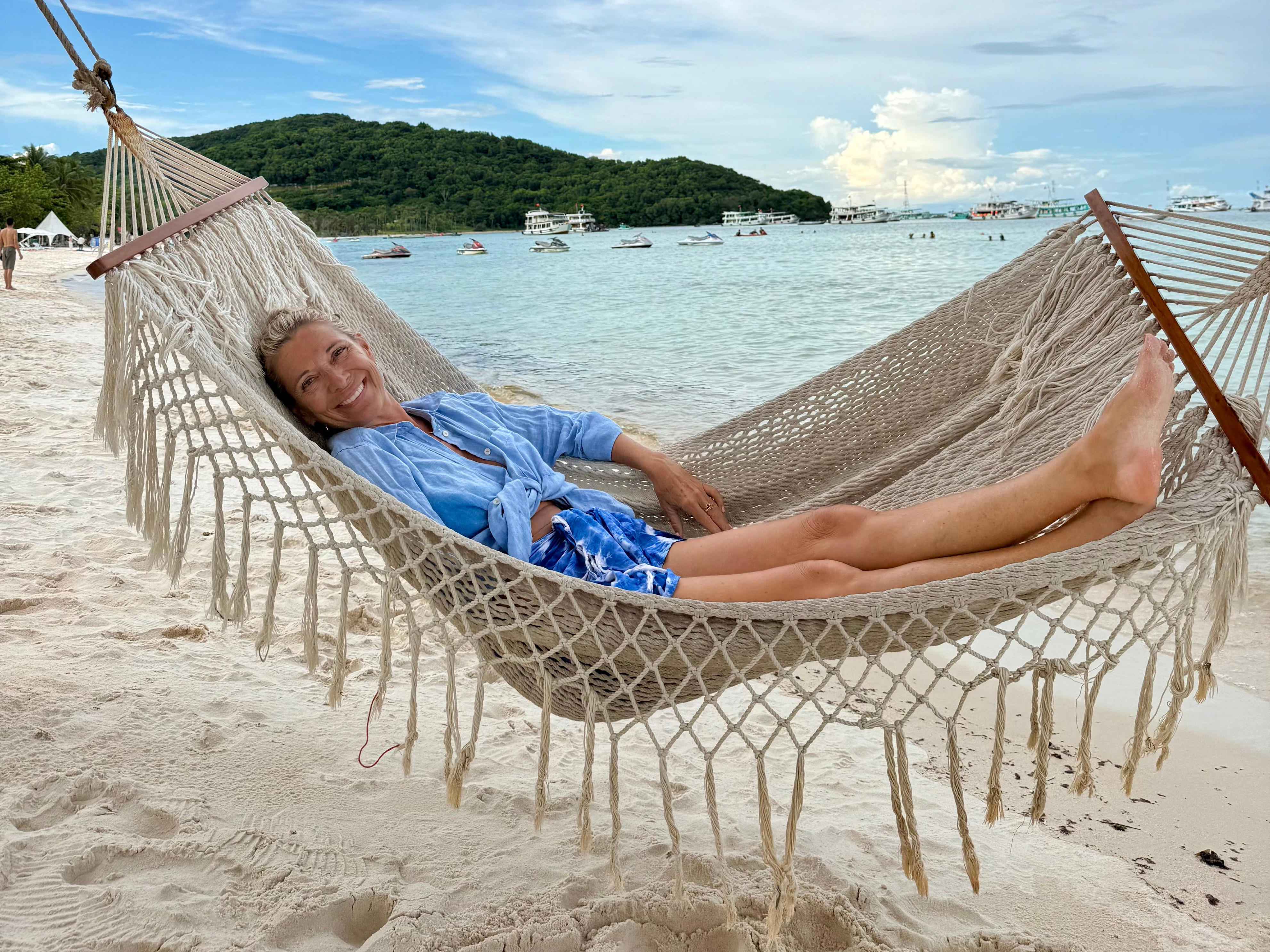 A woman lying on a hammock on the beach.